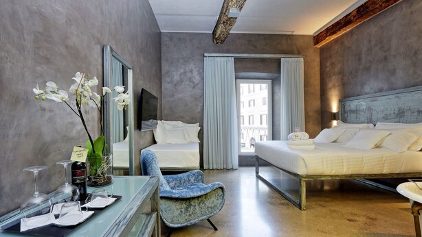 Habitación de hotel con cama, una silla, un escritorio y copas de vino, y vistas al exterior.