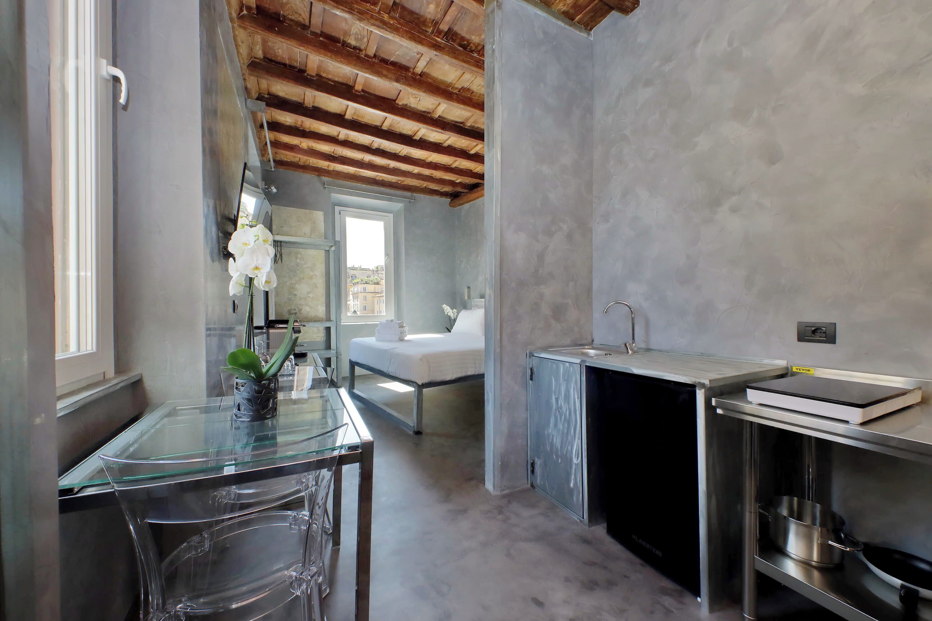 A compact kitchen with a glass table, a bed with a view, and a wooden ceiling.
