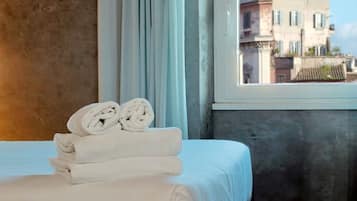 Een hotelkamer met een bed, een raam met gordijnen en uitzicht op gebouwen.