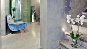 Un interior moderno con un arco de piedra, una silla azul y una orquídea en maceta sobre una escalera.