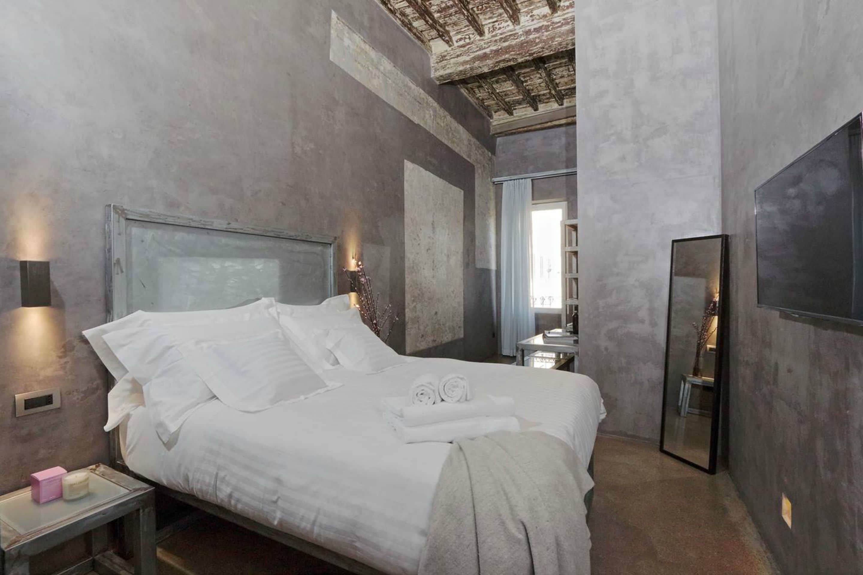 A modern bedroom with a large bed, bedside tables, a mirror, and a ceiling with exposed beams.