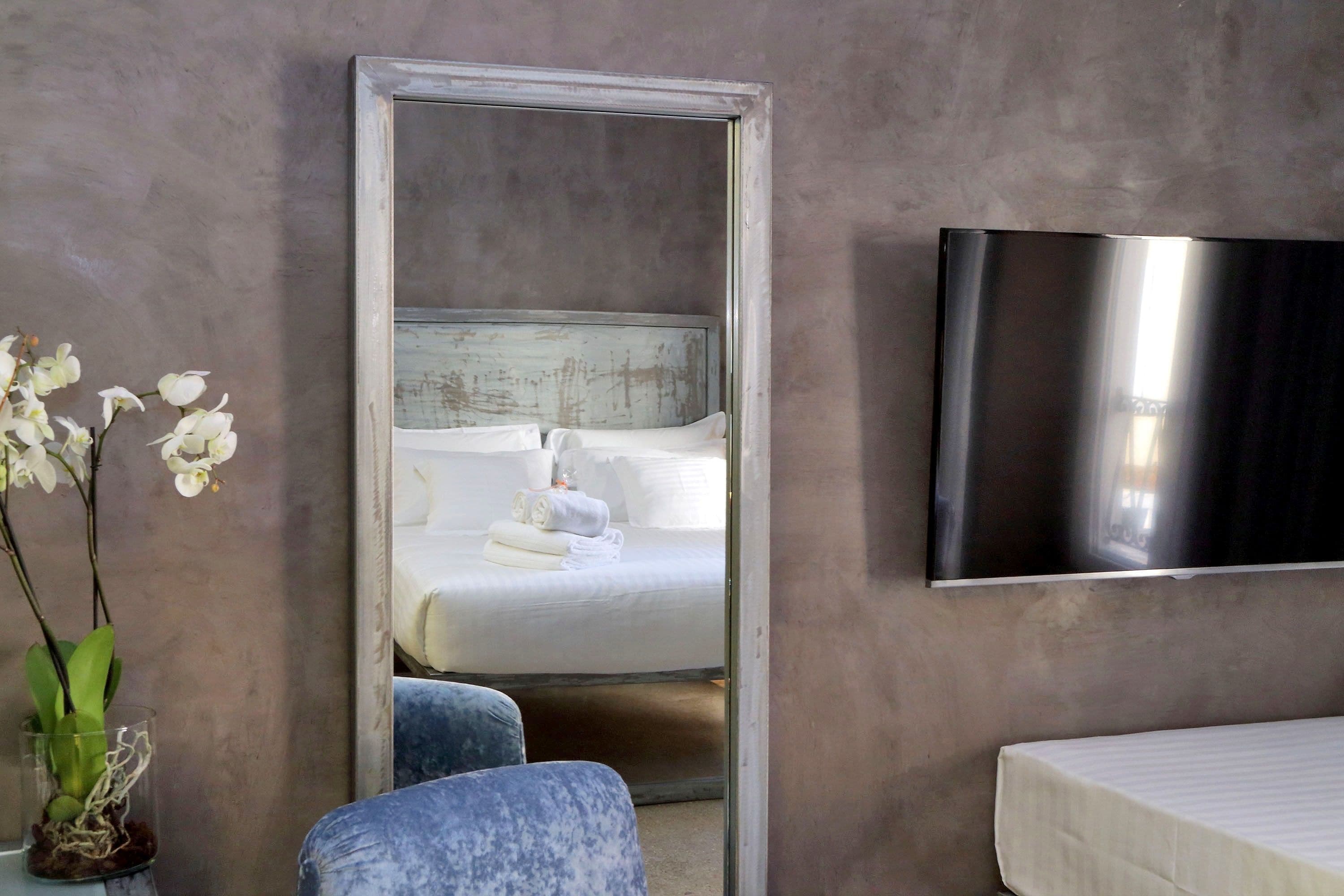 Une chambre d’hôtel avec un lit, un téléviseur fixé au mur, un miroir et un vase avec des fleurs.