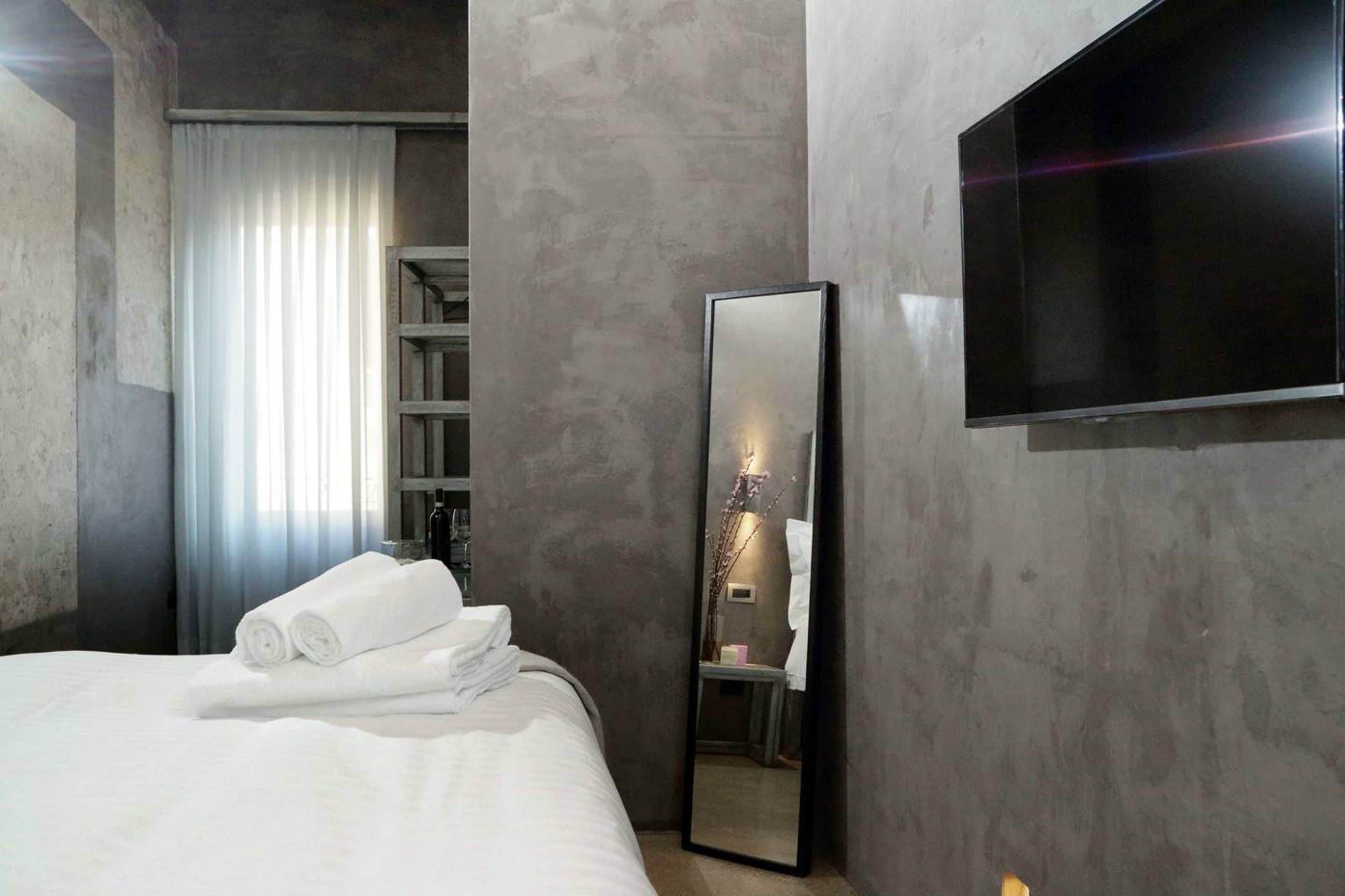 A modern hotel room with a large bed, a flat-screen TV, a mirror, and a wardrobe.