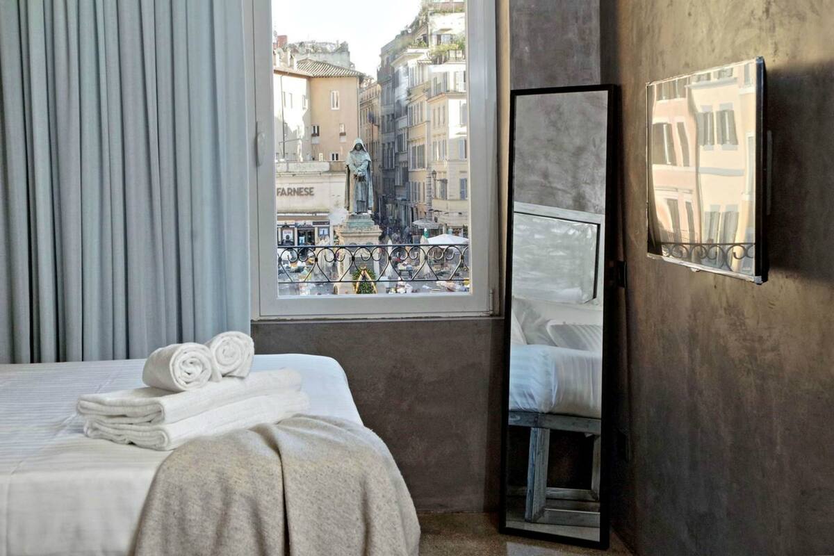 A hotel room with a bed, a window with a view of a cityscape, and a mirror on the wall.