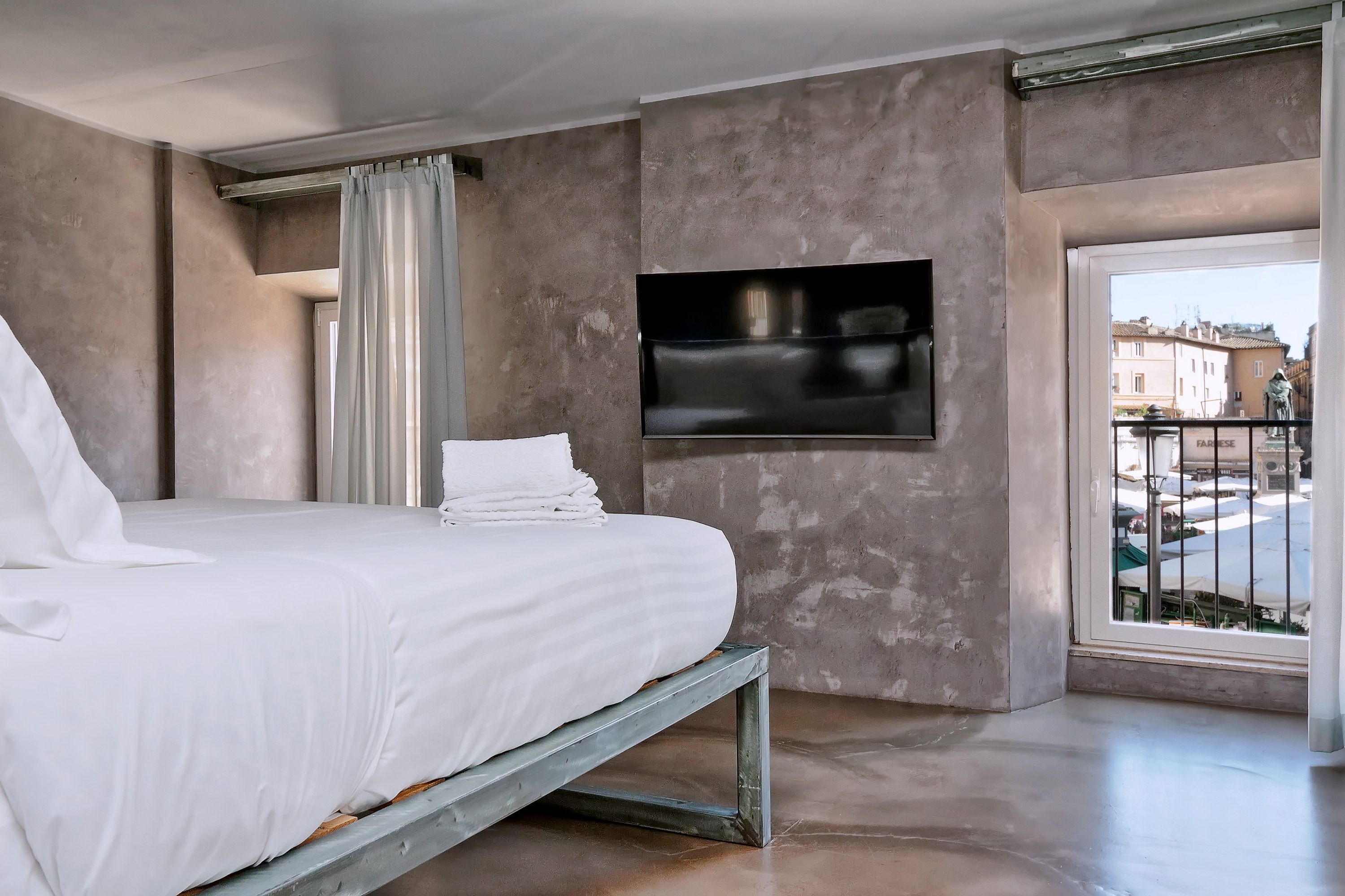 A bedroom with a bed, a TV mounted on the wall, and a view of the outside balcony.