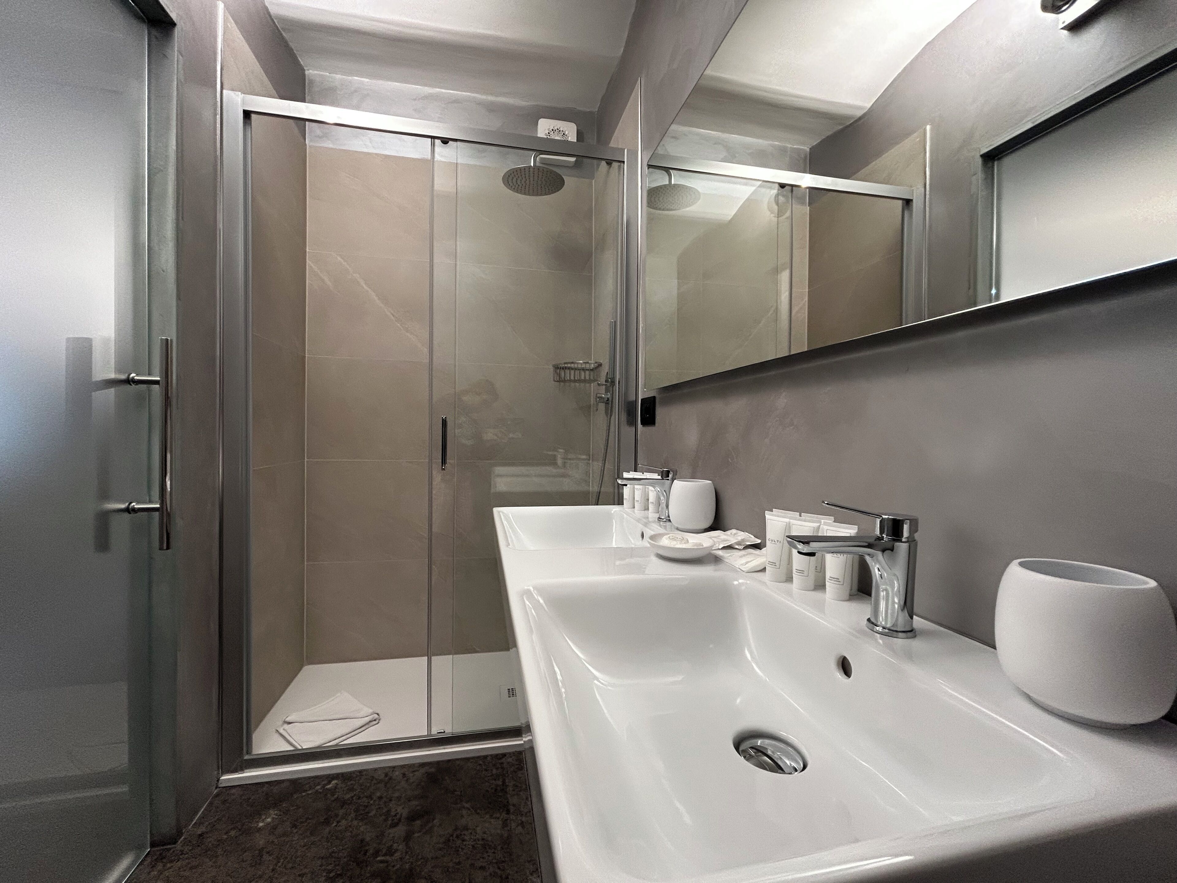 A modern bathroom with a glass-enclosed shower, a double sink with a mirror above, and a marble floor.