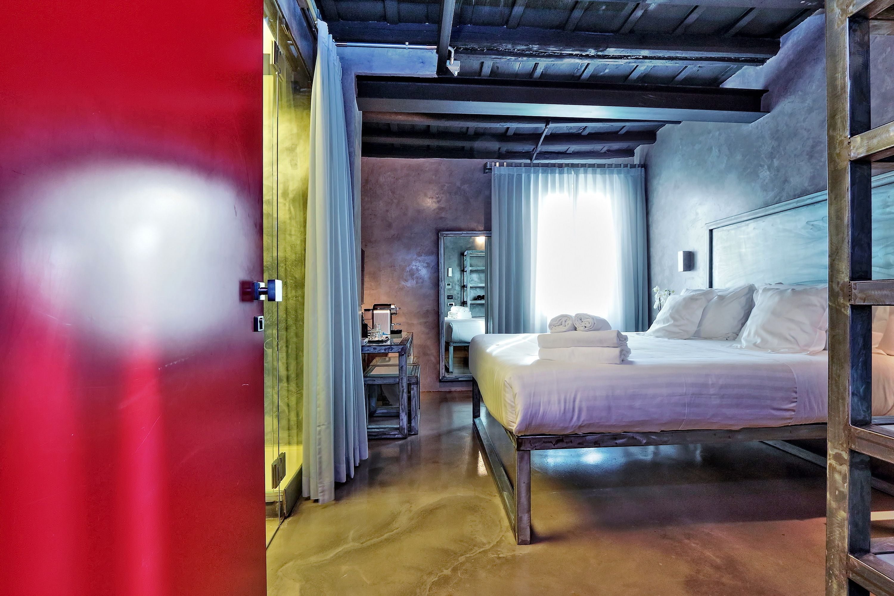 A bedroom with a bed, a nightstand, a mirror, and a window with curtains.