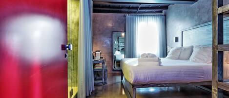 Un dormitorio con cama, mesita de noche, espejo y ventana con cortinas.