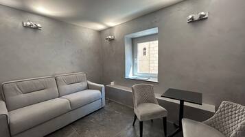 A modern, minimalist room with a grey sofa, two armchairs, a small table, and a window with a view of a building.