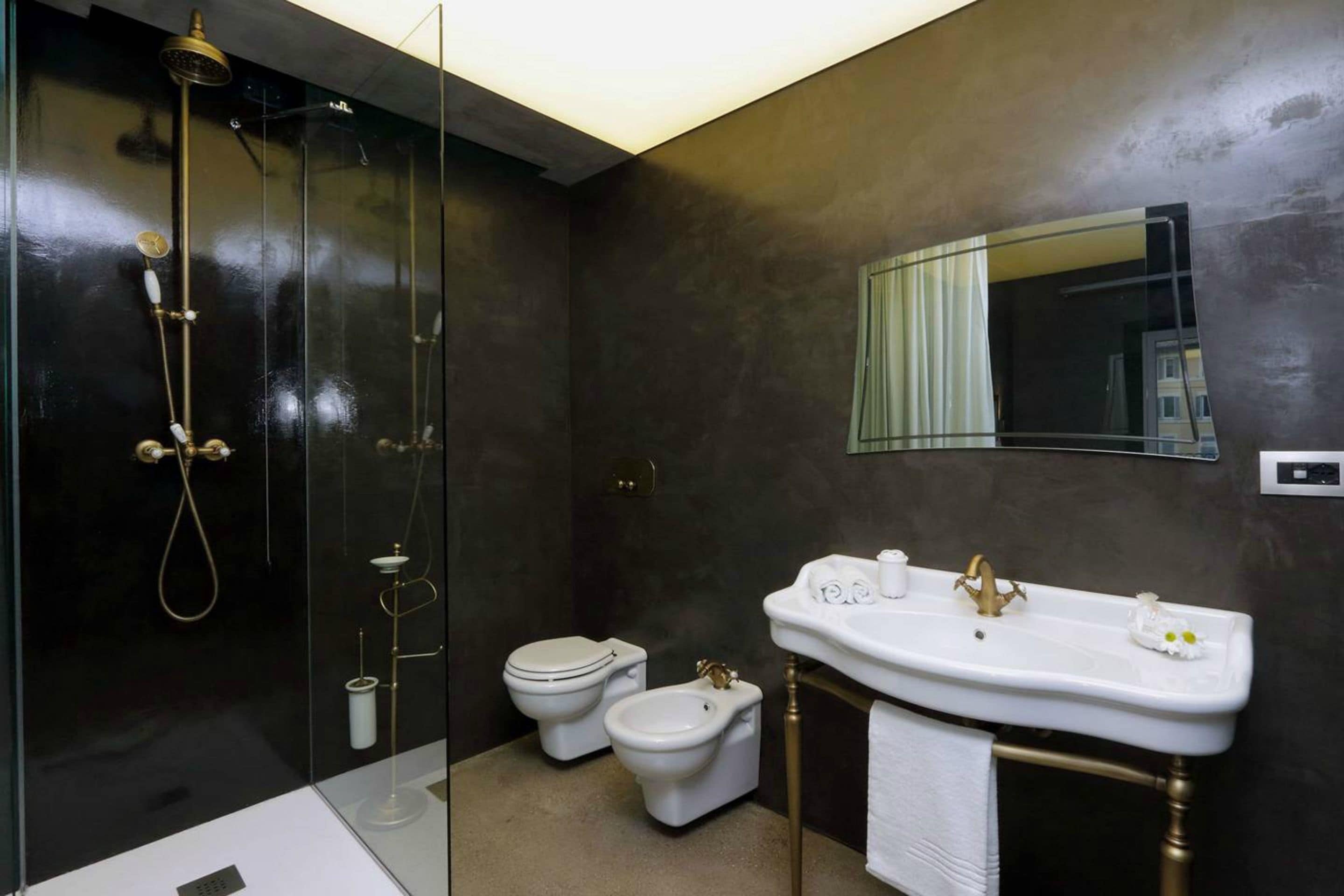 A modern bathroom with a glass-enclosed shower, a white sink with gold fixtures, and a toilet.