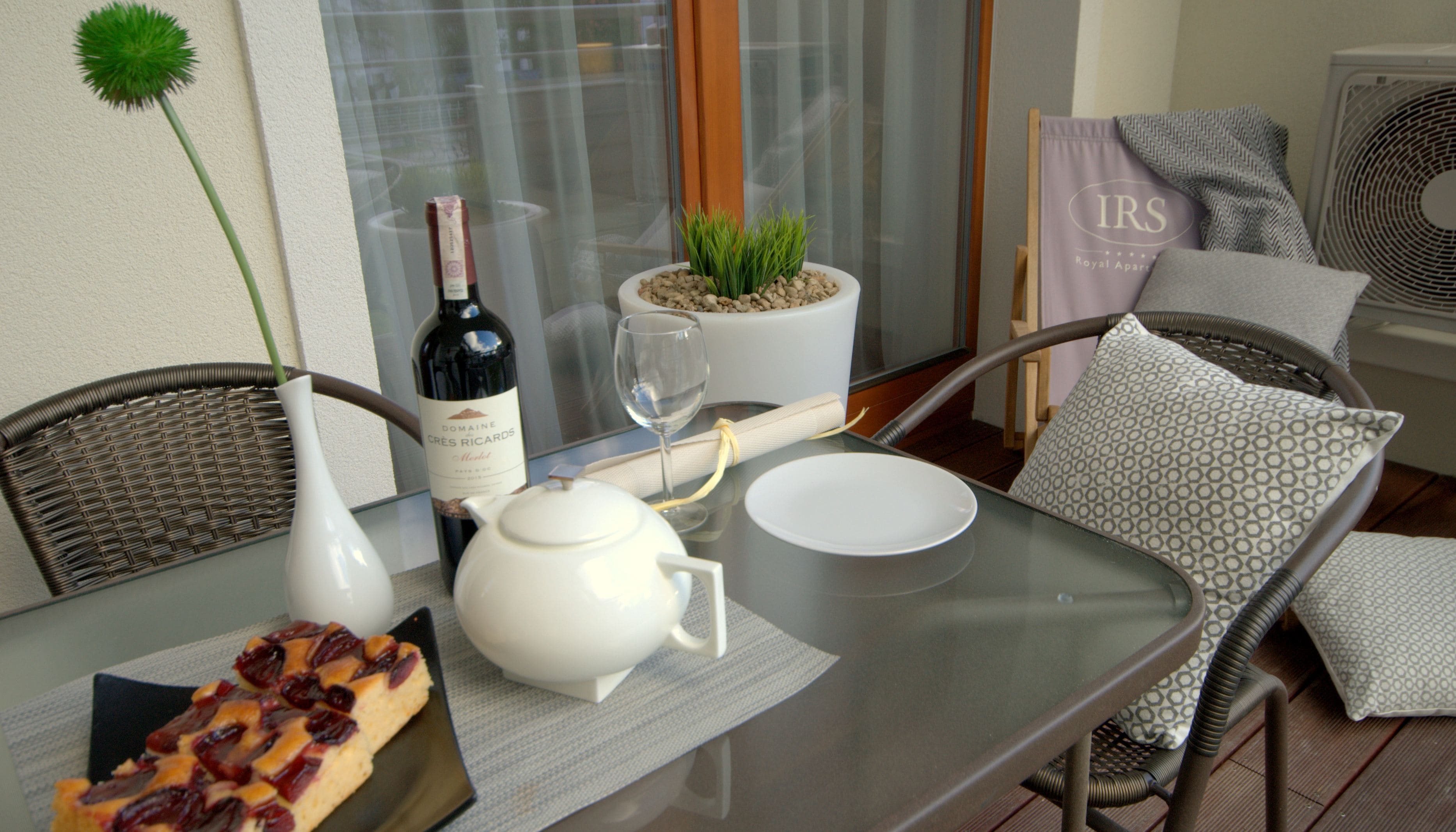 A dining table with a bottle of wine, a glass, a teapot, and a plate of food.