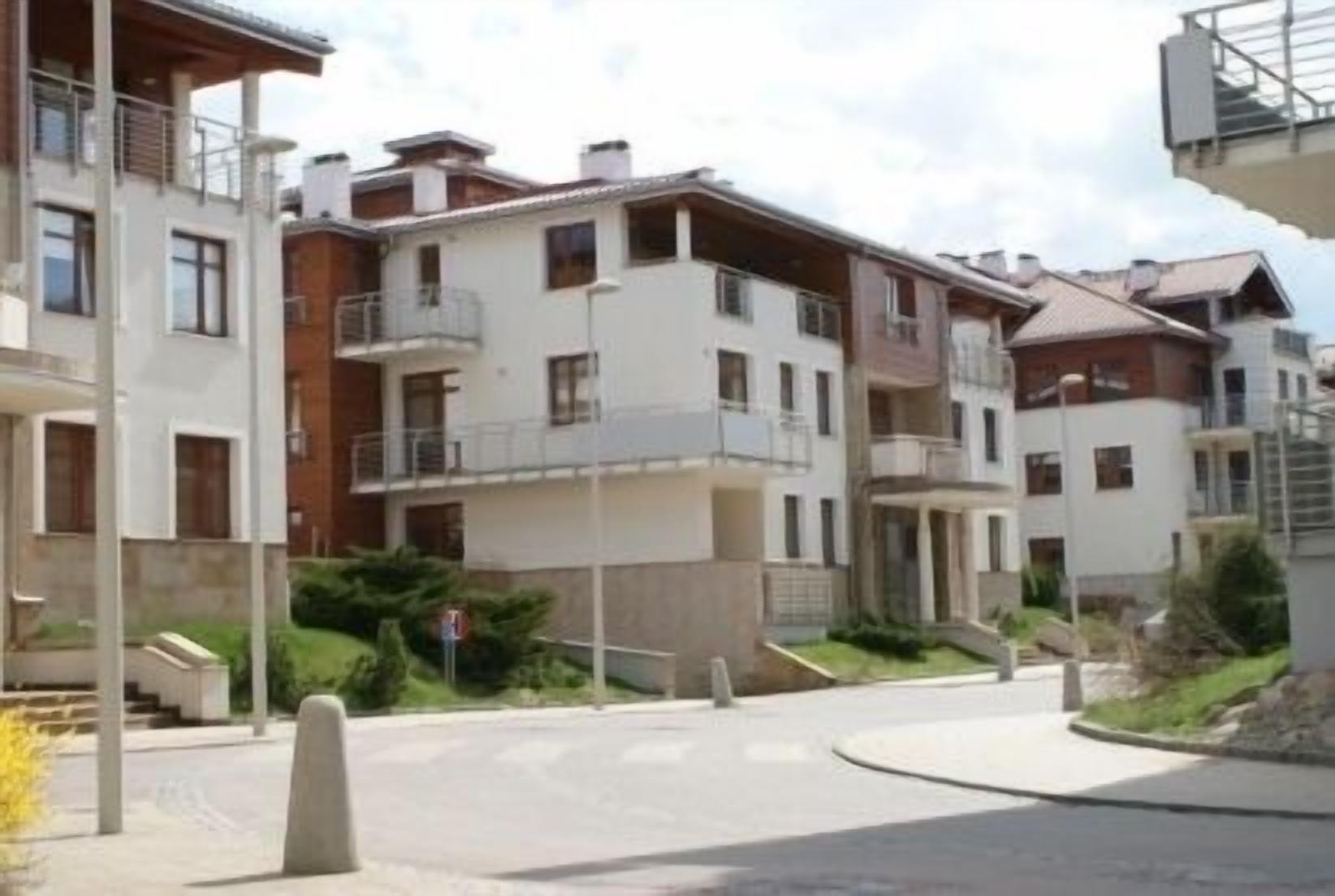 Un edificio residencial con varios balcones, entrada protegida y camino de acceso pavimentado.