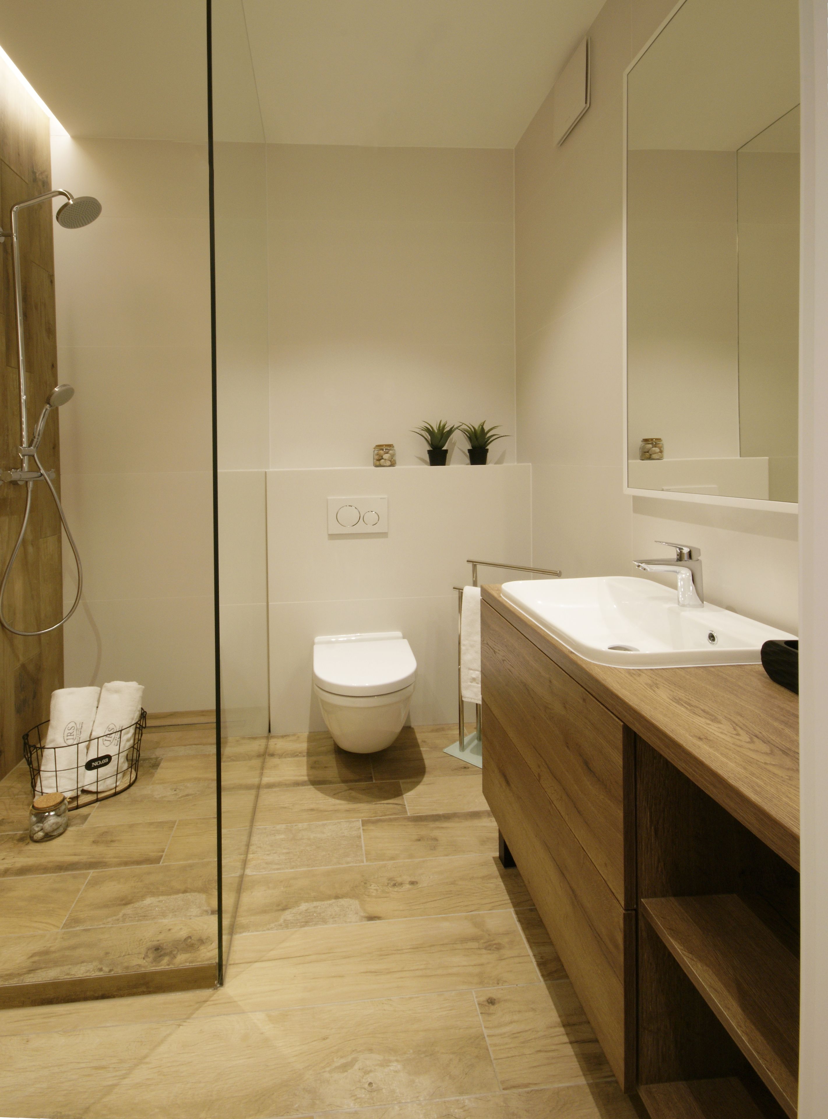 Un baño moderno con cabina de ducha de vidrio, inodoro blanco y tocador de madera con lavabo.