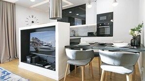 A modern kitchen with a built-in TV, wooden flooring, and a dining area with grey chairs. - IRS ROYAL APARTMENTS - IRS Neptun Park (Gdansk)