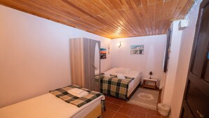 A bedroom with two beds, wooden ceiling, and a small bedside table with a lamp. - Istanbul Pansiyon (Ayvalik)