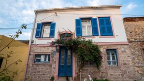 A two-story building with a blue door and shutters, a stone facade, and a small porch with a white chair. - Istanbul Pansiyon (Ayvalik)