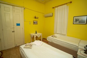A room with two beds, a small table, an air conditioning unit, and a door. - Istanbul Pansiyon (Ayvalik)