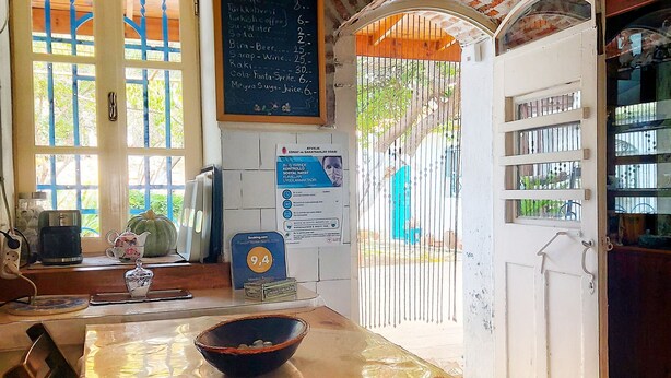 A dining area with a wooden table, chairs, a bowl, a teapot, and a menu board. - Istanbul Pansiyon (Ayvalik)