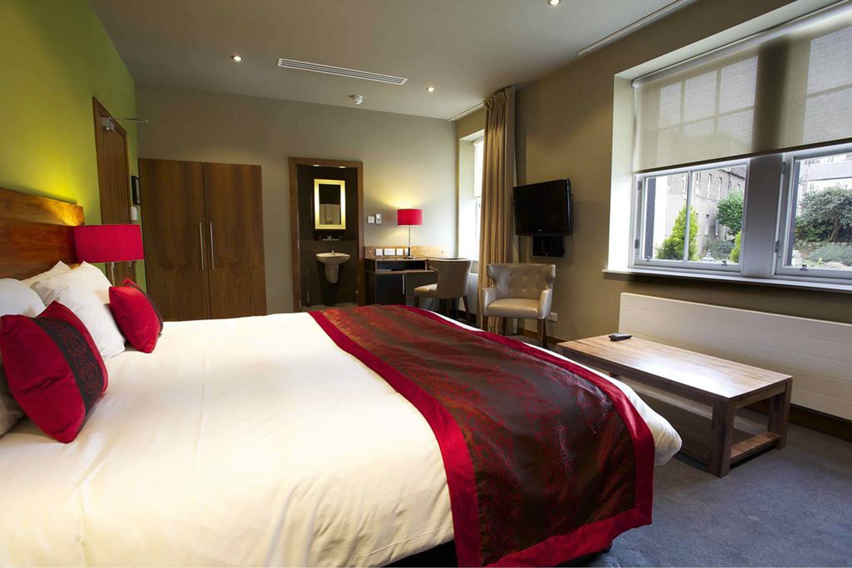 A hotel room with a bed, a desk, a chair, a TV, and a window.