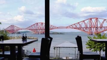 Vista de un puente rojo sobre el agua, tomada desde un restaurante con mesas y sillas.