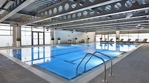 Ein großer, überdachter Pool mit klarem, blauem Wasser, umgeben von Liegestühlen und einer hohen Decke mit Rundöffnungen.