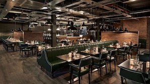 Un restaurante con asientos tipo cabina verdes, mesas de madera y lámparas colgantes.