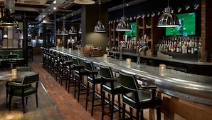Una zona de bar con una barra larga, varios taburetes y una gran variedad de botellas y vasos.