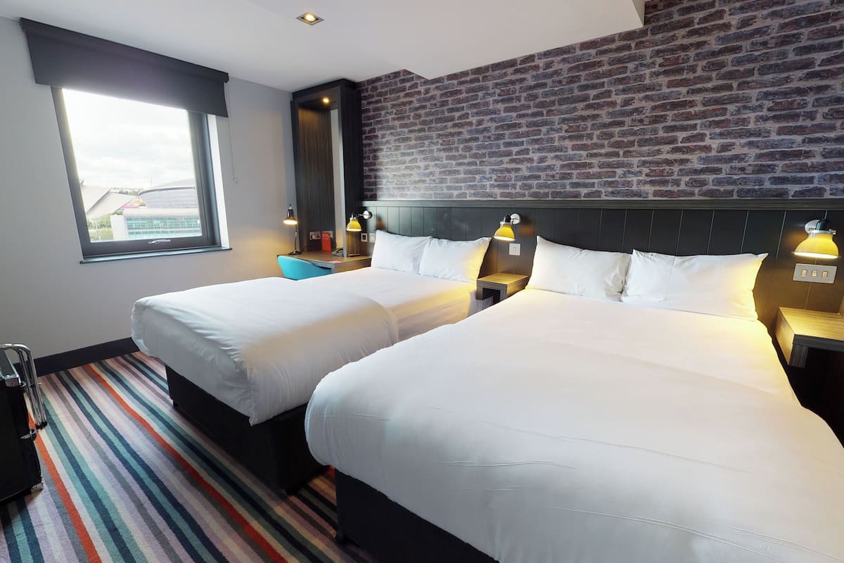 A hotel room with two beds, a brick wall, a large window, and a striped carpet.