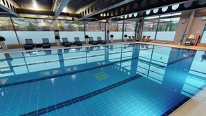 Una piscina interior con agua cristalina, tumbonas y vistas a edificios.