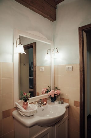Un baño con un lavamanos blanco, un espejo y dos luces fijadas a la pared.