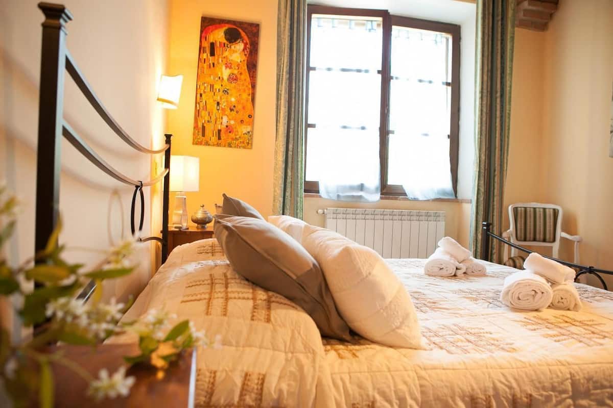 Ein Hotelzimmer mit Bett, Vorhängen am Fenster, Heizkörper, Stuhl und einem Bild an der Wand.