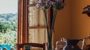A dining table with a vase of flowers, a pitcher, and a rustic setting with a view of greenery outside. - Il Vecchio Mulino Farmhouse (Radicondoli)