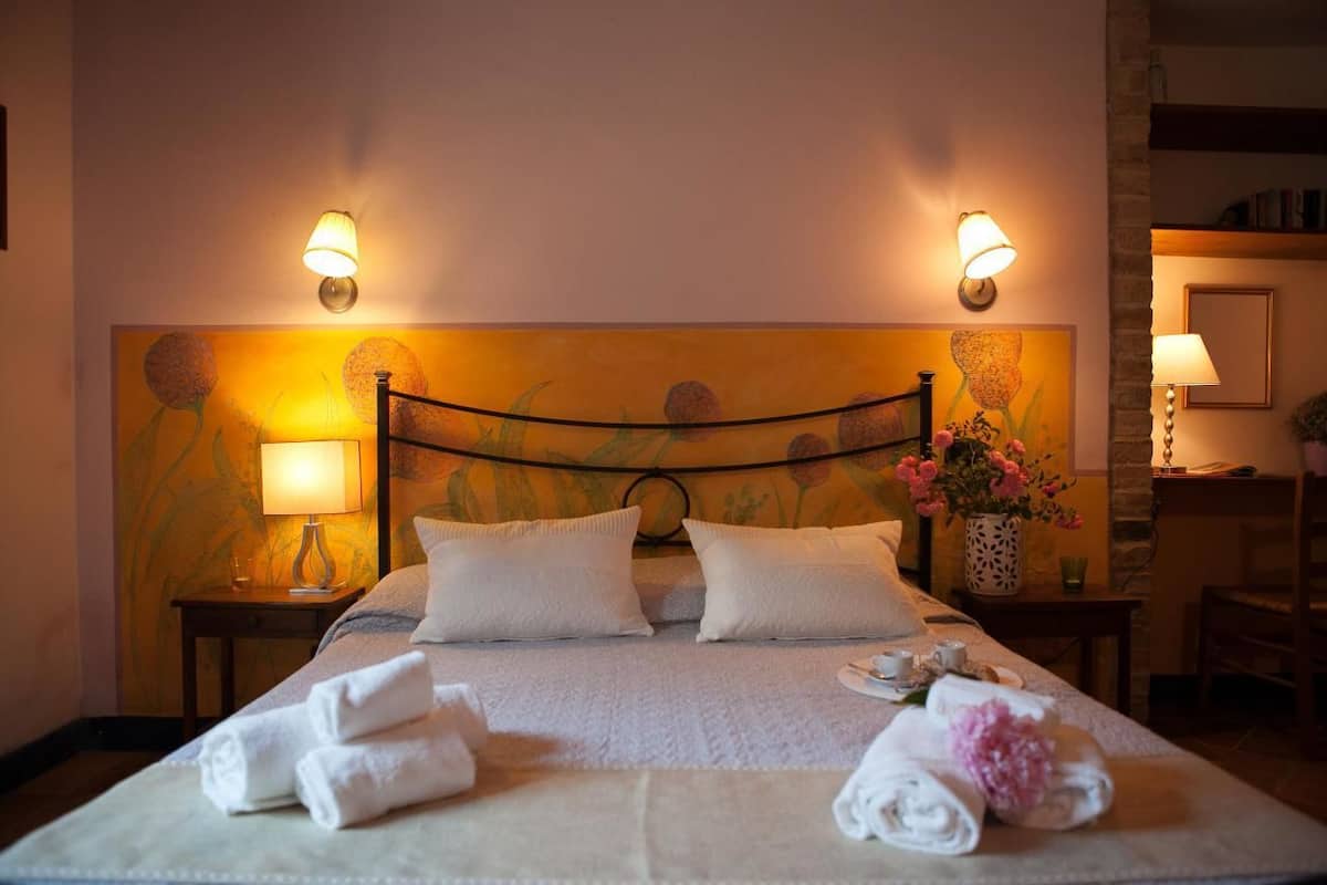 Ein ordentlich bezogenes Bett mit weißen Leinen und Handtüchern, zwei Wandlampen und ein Blumenbild an der Wand.