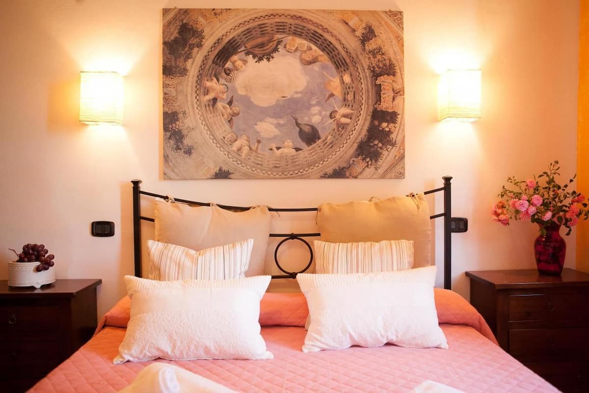Ein Bett mit einer rosa Bettdecke, zwei weißen Kissen und einem Kopfteil mit kreisförmigem Design. An beiden Seiten des Bettes befinden sich zwei Wandlampen.