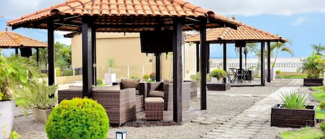 A covered outdoor seating area with wicker furniture and a small round green bush.