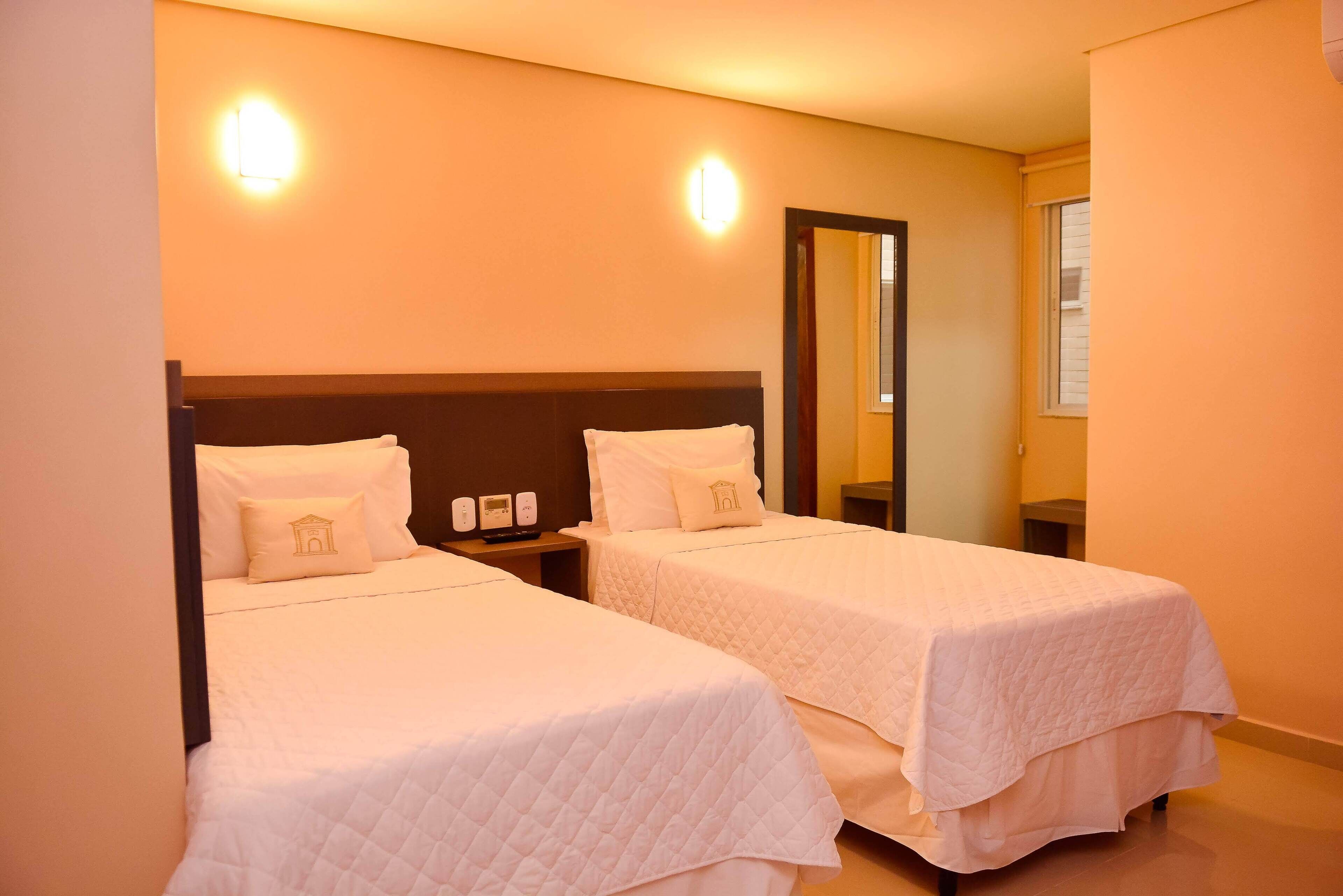 Two single beds with white bedding, a nightstand with a phone and a lamp, and a large mirror on the wall.