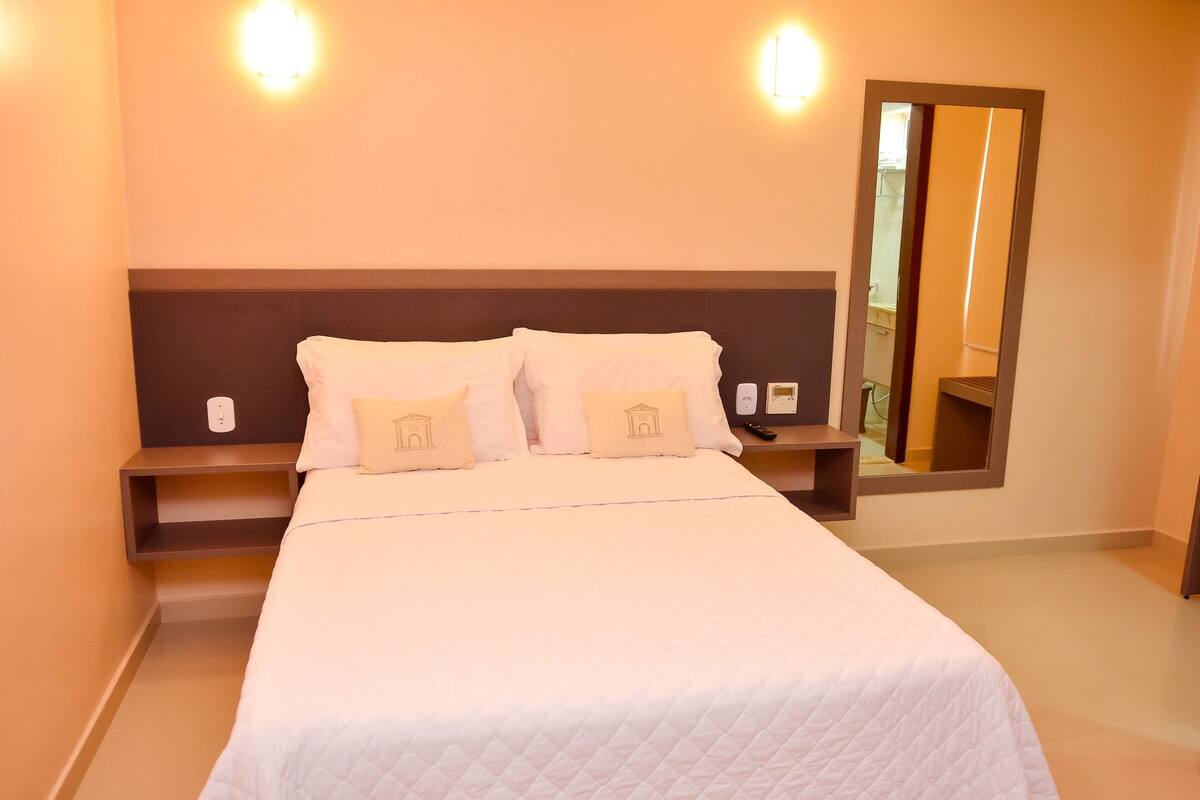 Une chambre d’hôtel avec un grand lit, deux tables de chevet, une petite table et un miroir au mur.