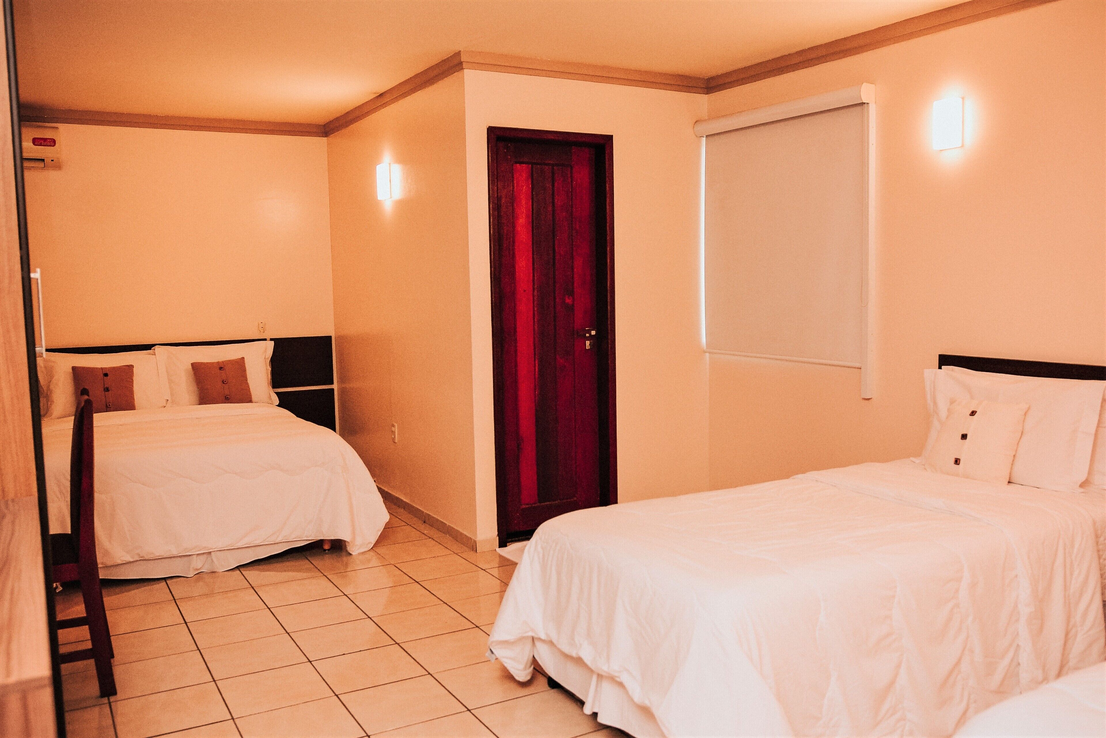 A hotel room with two beds, a wooden door, and a window.