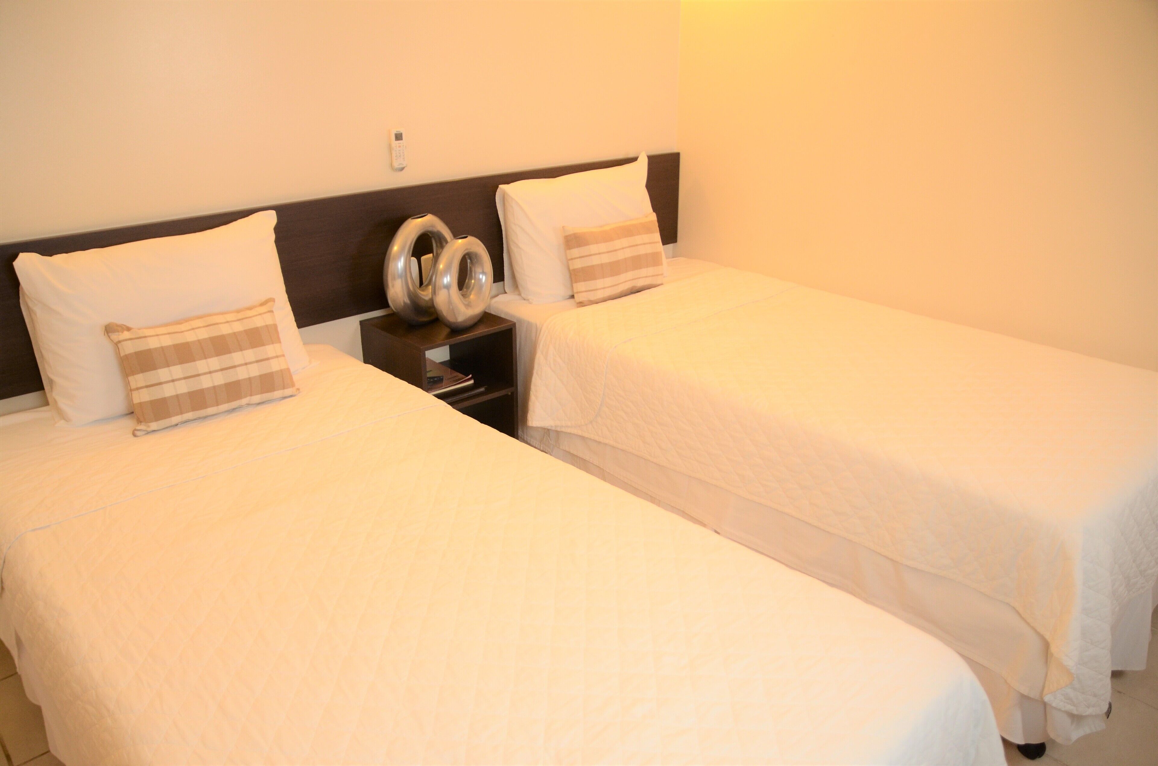Two single beds with white bedding and a headboard, a bedside table with a lamp, and a wall-mounted phone.