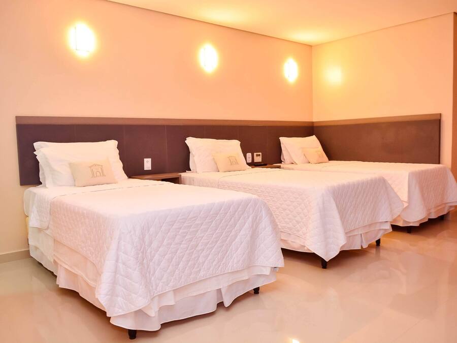Two single beds with white bedding and headboards, a wall-mounted light fixture, and a clean, tiled floor.