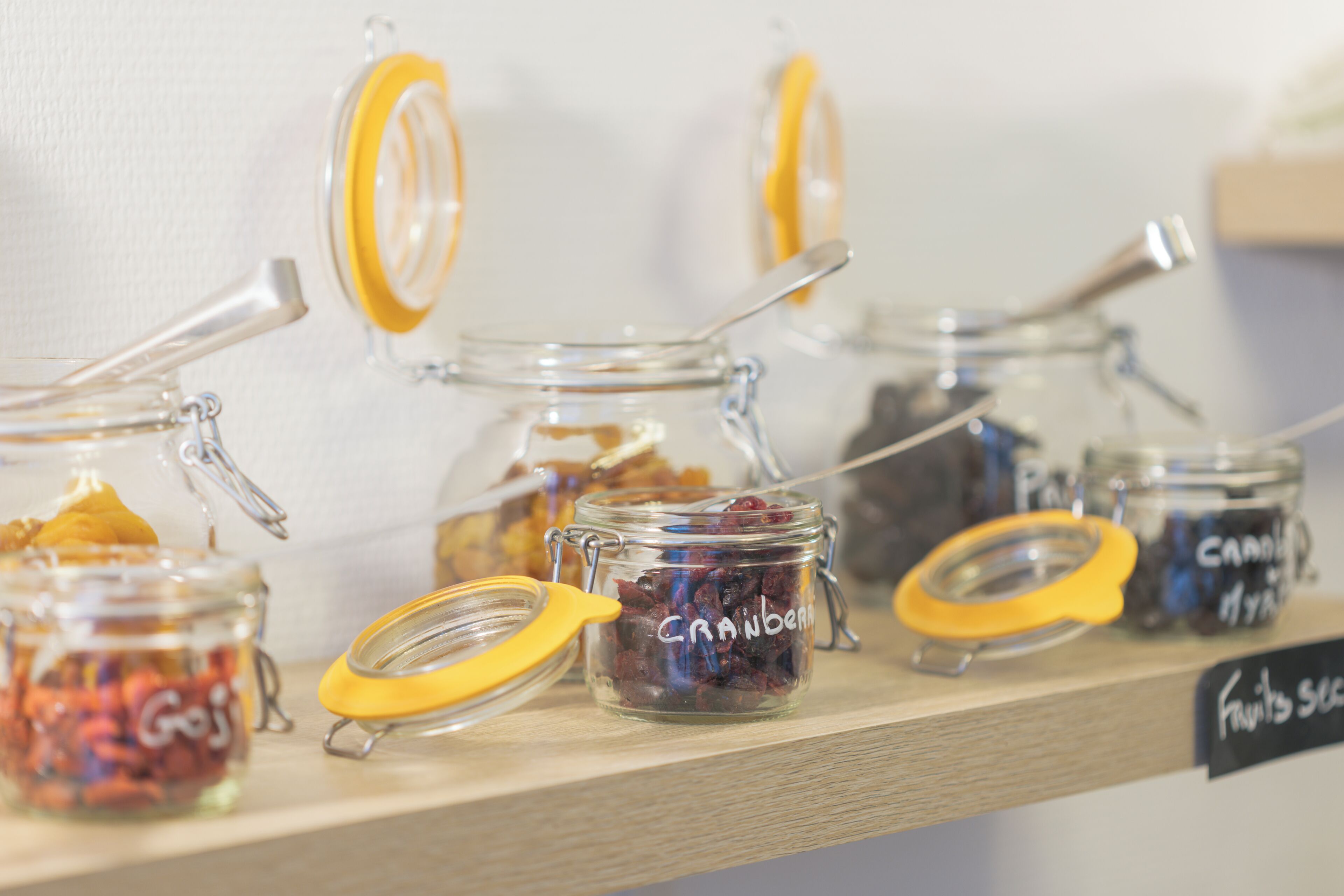 A shelf with multiple glass jars containing various dried fruits, each labeled with its contents.