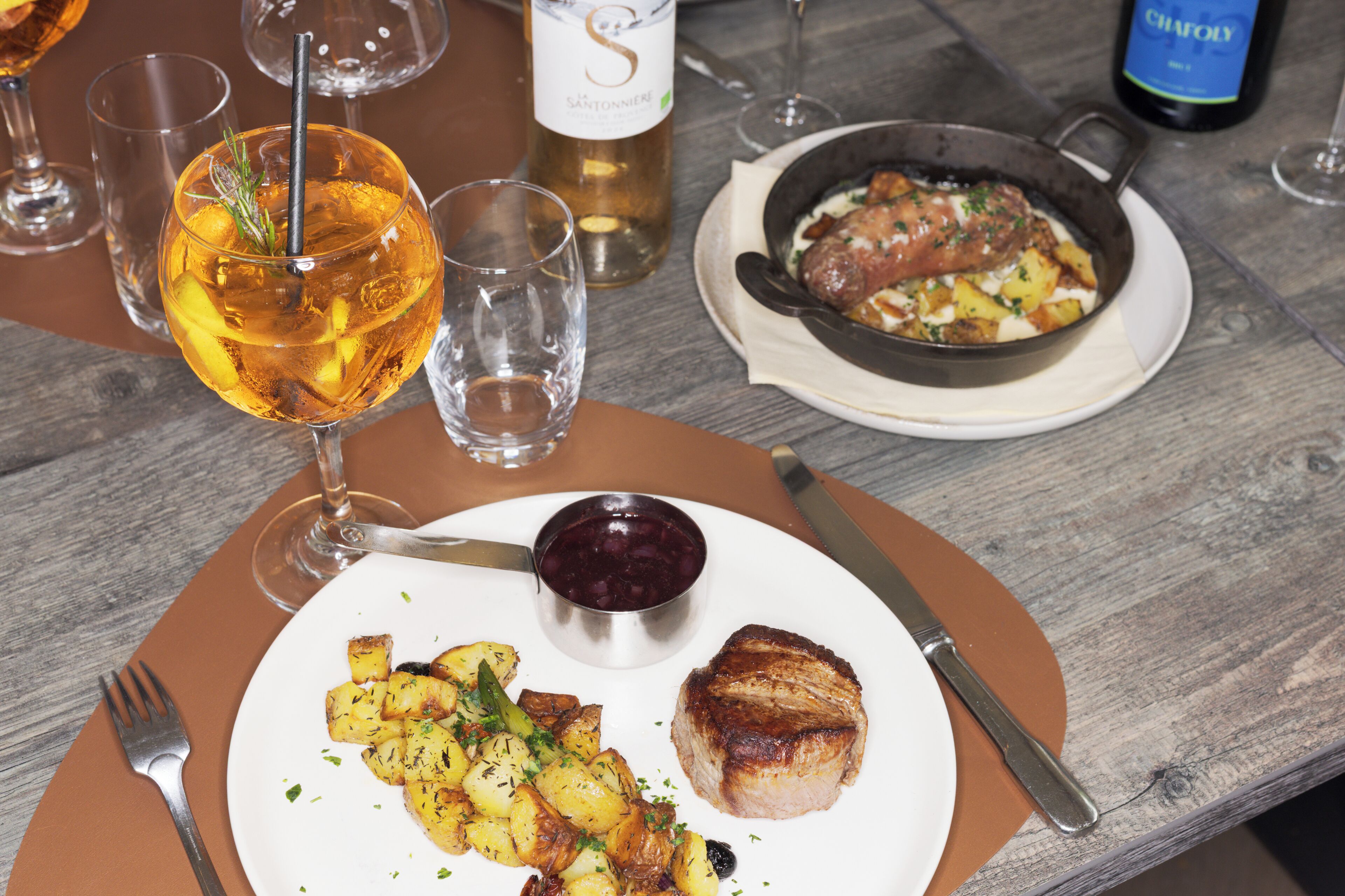 Una mesa de comedor con un plato de comida, un vaso de bebida color ámbar y una botella de vino.