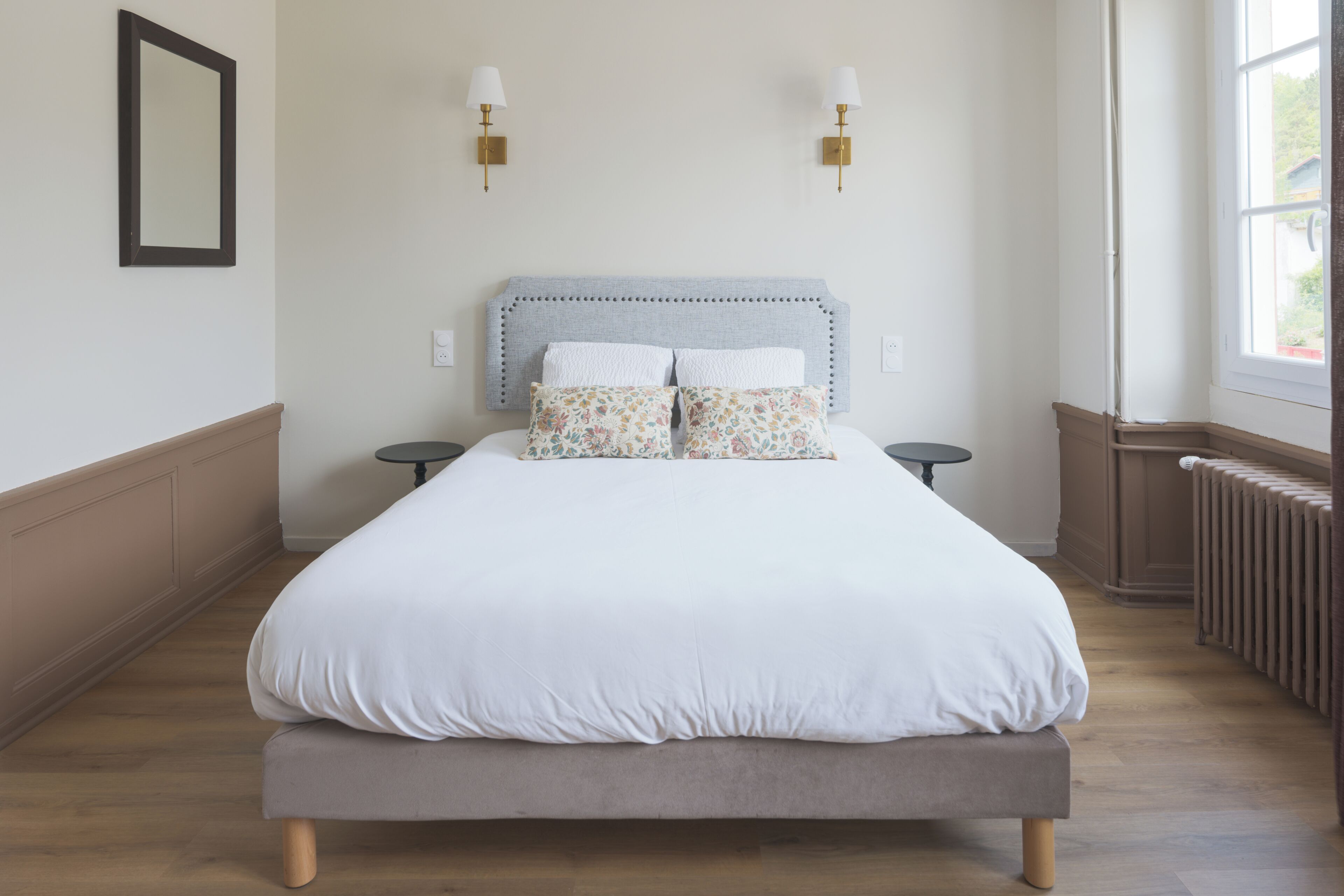 Un dormitorio con cama, dos apliques, un radiador y una ventana.