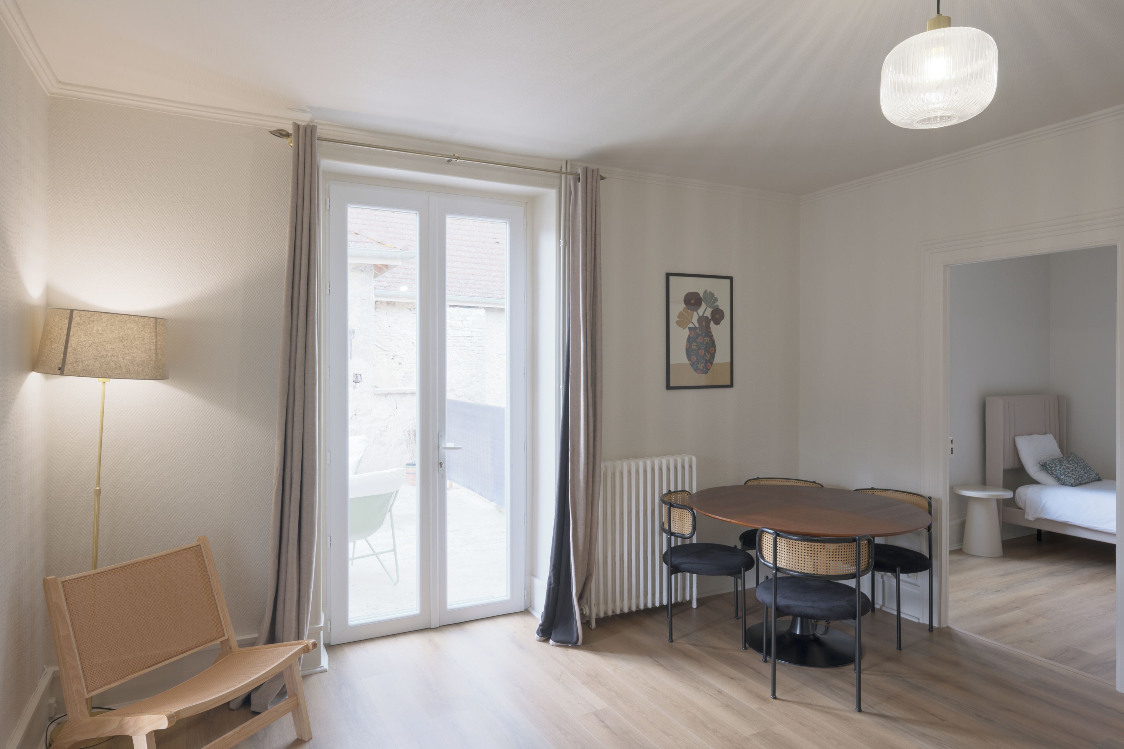 A room with a dining table, chairs, a bench, a lamp, a radiator, and a door leading to an outdoor area.