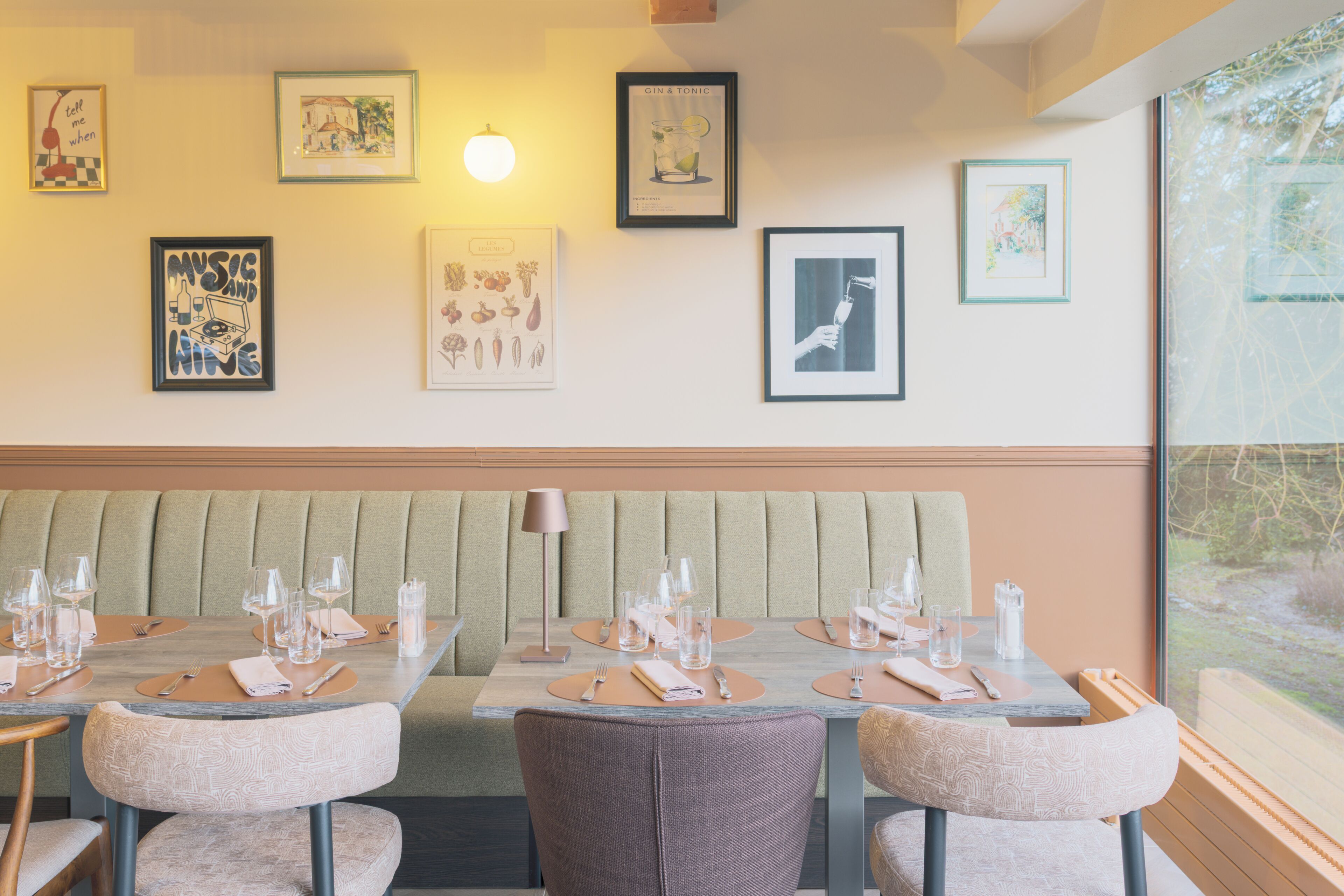 A dining area with tables set for four, a cushioned bench, and framed artwork on the walls.
