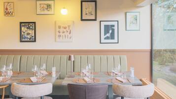 A dining area with tables set for four, a cushioned bench, and framed artwork on the walls.