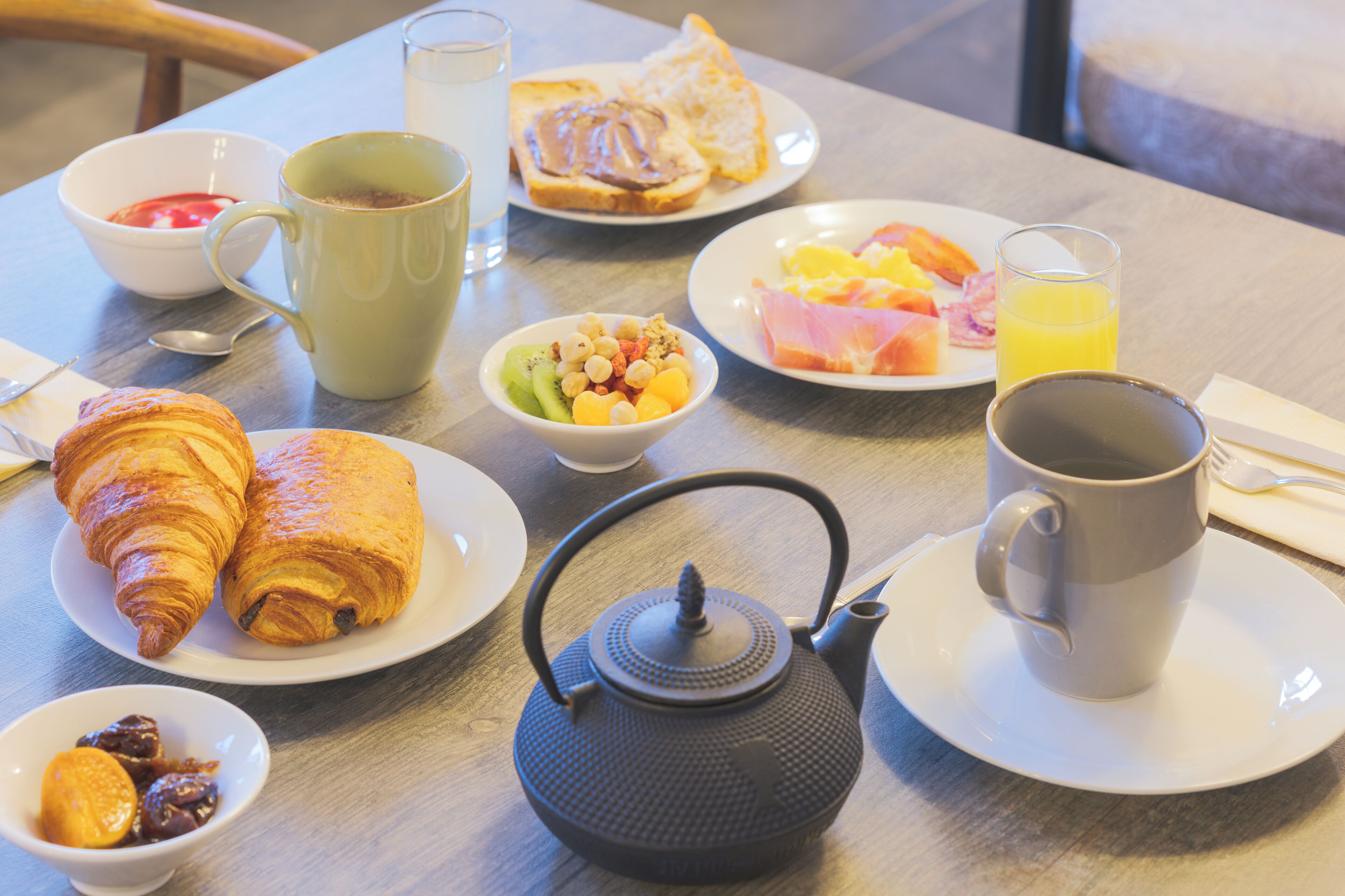 Et morgenbord med croissanter, frugt, en tepotte og en kop.