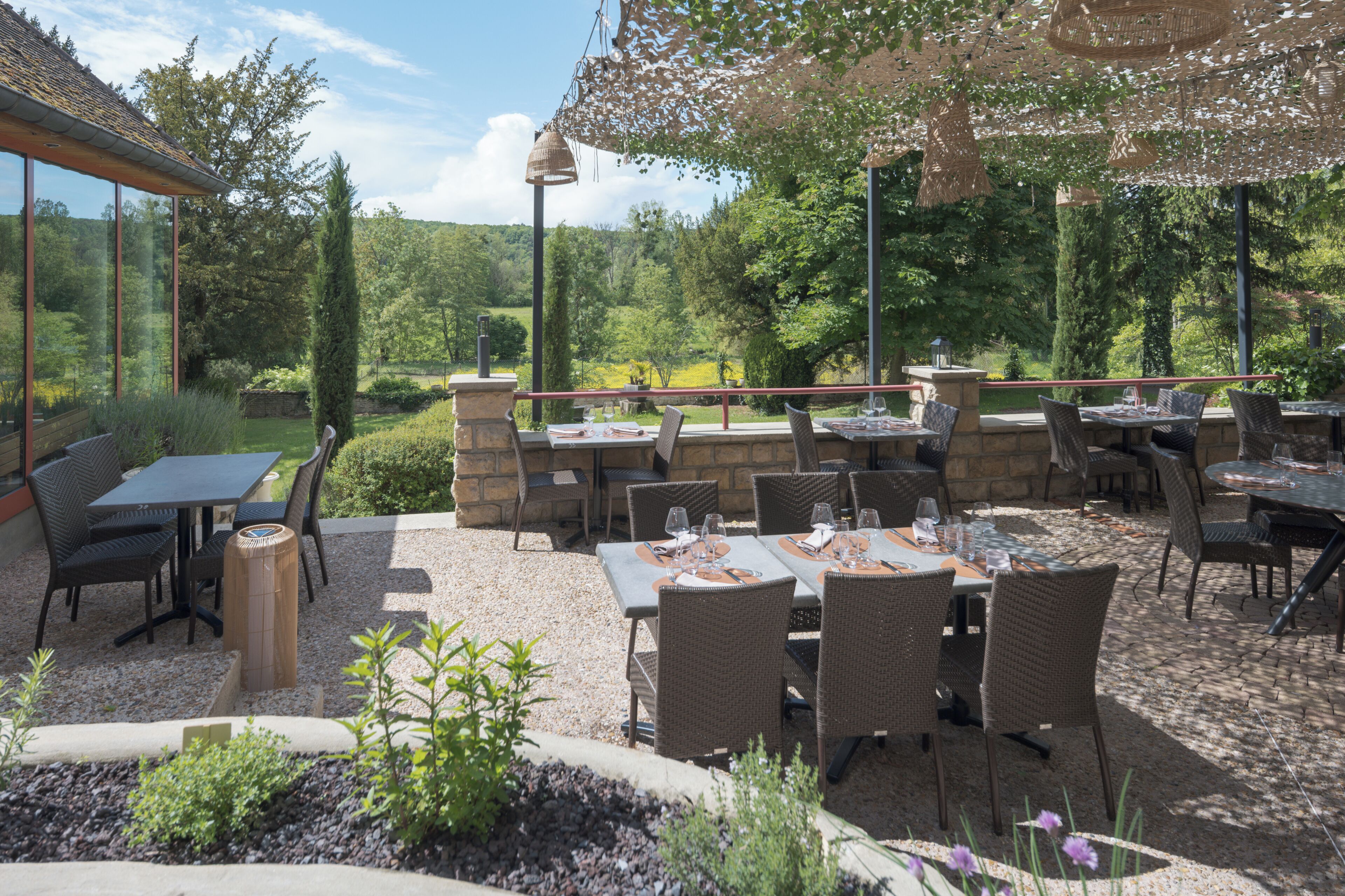 Une terrasse extérieure avec des tables et des chaises, entourée d’un mur en pierre et de panneaux de verre.