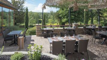 Une terrasse extérieure avec des tables et des chaises, entourée d’un mur en pierre et de panneaux de verre.