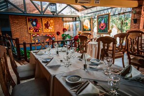 A restaurant with a long table set for dining, surrounded by chairs, and decorated with flowers.